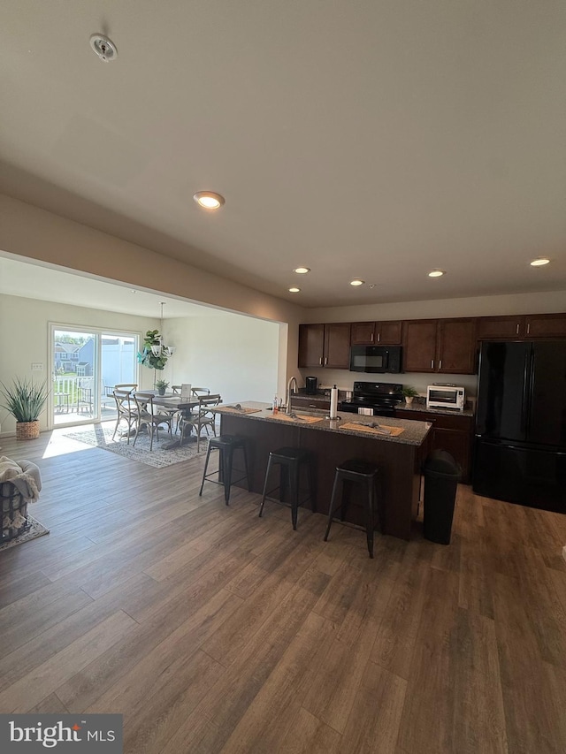 kitchen featuring a breakfast bar area, recessed lighting, dark brown cabinetry, wood finished floors, and black appliances