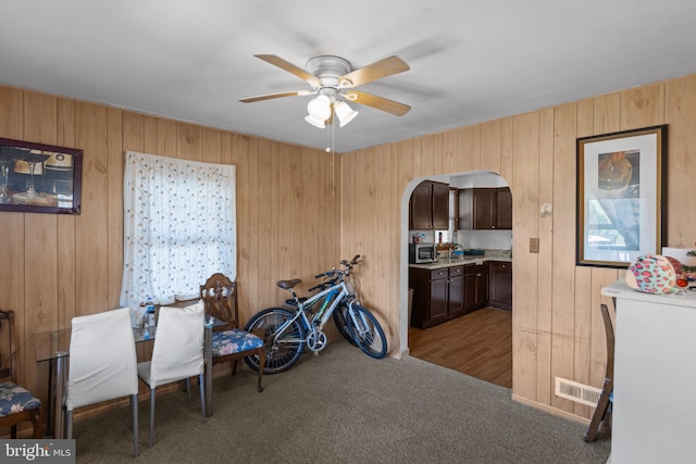 miscellaneous room with arched walkways, ceiling fan, wooden walls, and carpet flooring