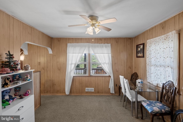 dining room featuring a ceiling fan, carpet flooring, and wood walls