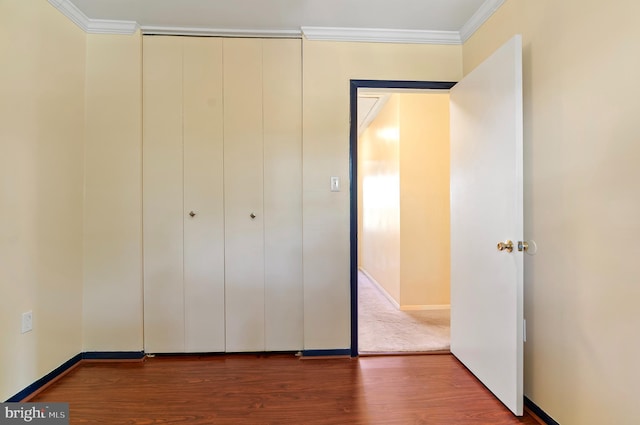 unfurnished bedroom with crown molding, baseboards, a closet, and wood finished floors