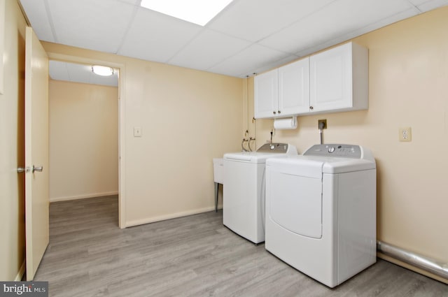 washroom with washing machine and clothes dryer, baseboards, light wood-style flooring, and cabinet space
