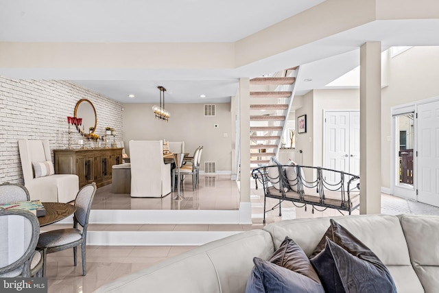 living room with stairway, tile patterned floors, brick wall, and visible vents