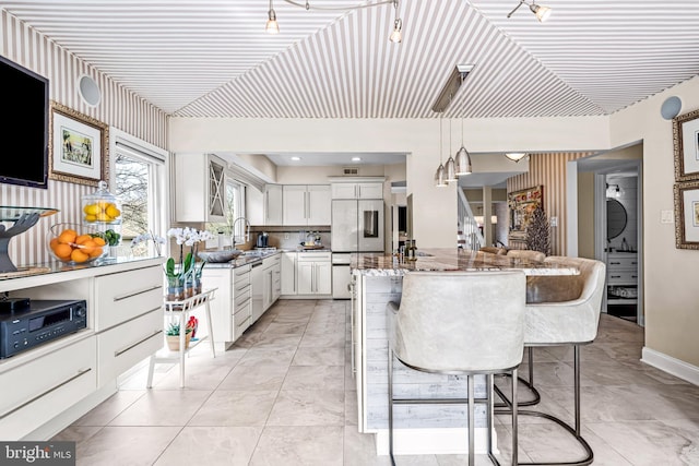 kitchen featuring light stone countertops, a sink, built in refrigerator, a breakfast bar, and white cabinetry