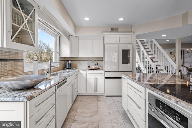 kitchen with appliances with stainless steel finishes, light stone counters, a sink, backsplash, and visible vents