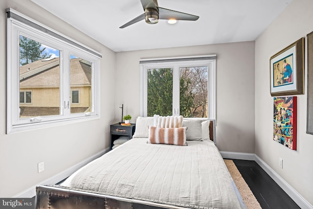 bedroom featuring baseboards, a ceiling fan, wood finished floors, and multiple windows