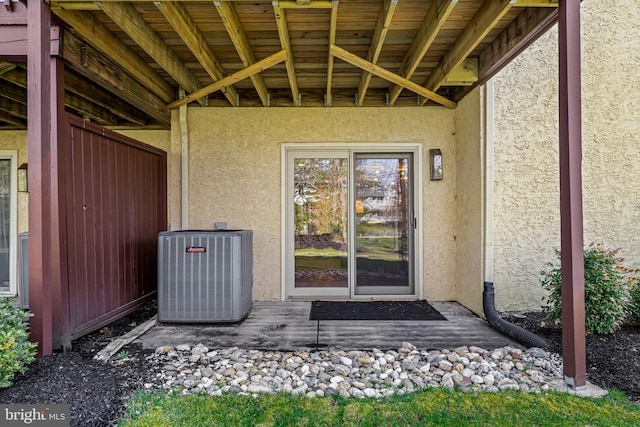 view of exterior entry featuring central air condition unit and stucco siding