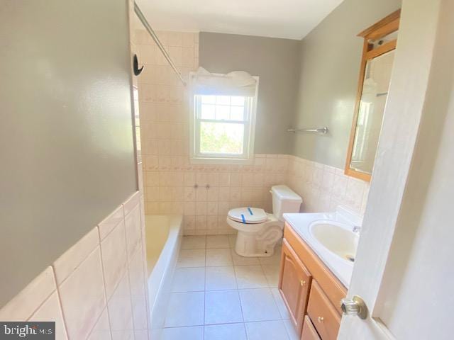 bathroom featuring wainscoting, tile patterned flooring, vanity, toilet, and tile walls