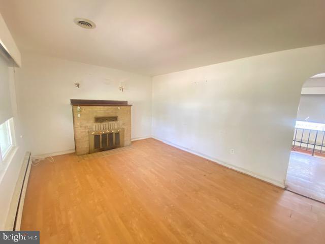 unfurnished living room featuring arched walkways, a brick fireplace, wood finished floors, baseboards, and a baseboard radiator