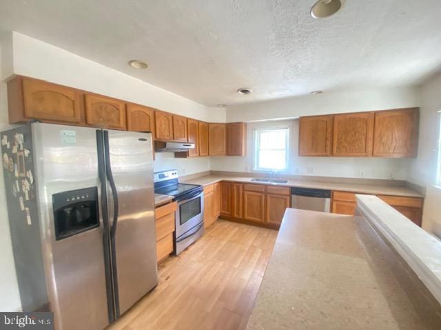 kitchen featuring a sink, light countertops, light wood finished floors, under cabinet range hood, and stainless steel appliances
