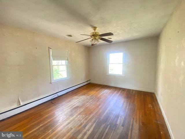 unfurnished room featuring baseboards, a baseboard heating unit, a wealth of natural light, and wood finished floors