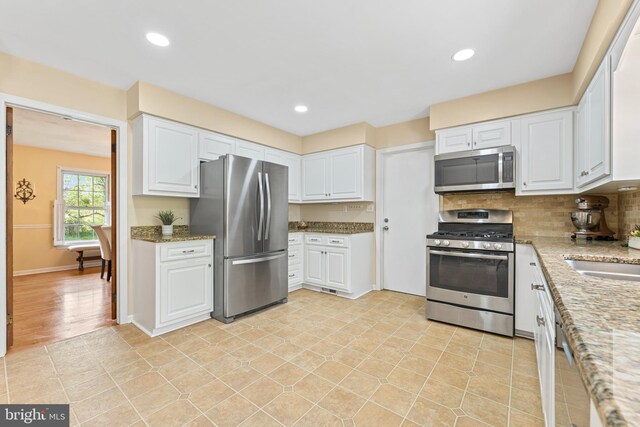 kitchen with backsplash, white cabinetry, light stone countertops, and appliances with stainless steel finishes