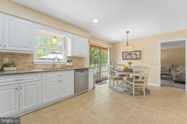 kitchen featuring hanging light fixtures, tasteful backsplash, stainless steel dishwasher, a sink, and white cabinetry