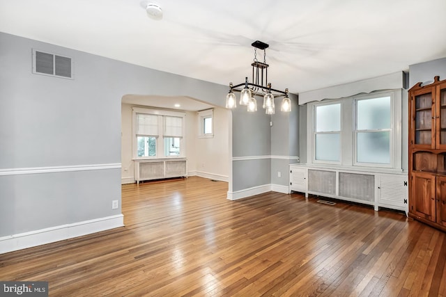 unfurnished dining area featuring wood-type flooring, arched walkways, and baseboards