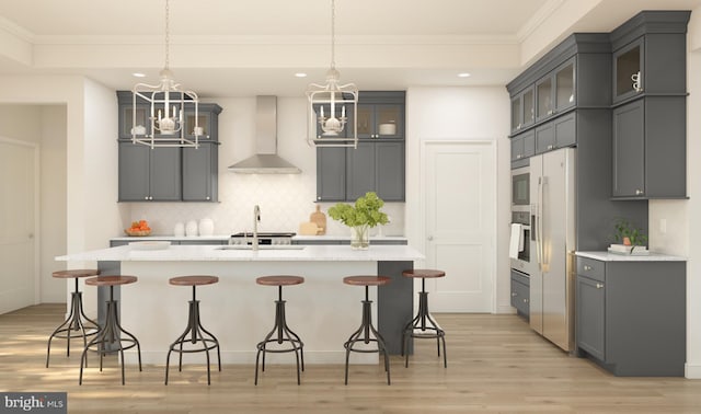 kitchen featuring wall chimney range hood, decorative backsplash, light wood-style floors, and a notable chandelier