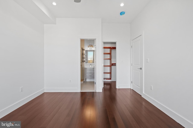unfurnished bedroom with baseboards, ensuite bathroom, a walk in closet, recessed lighting, and dark wood-type flooring