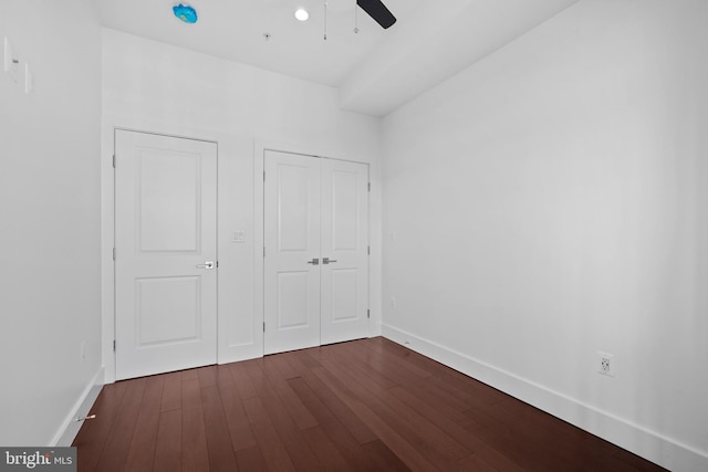 unfurnished bedroom featuring baseboards, a ceiling fan, dark wood-style flooring, and a closet