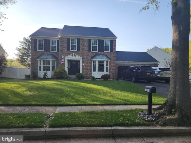 colonial home with brick siding, fence, a front yard, and a garage