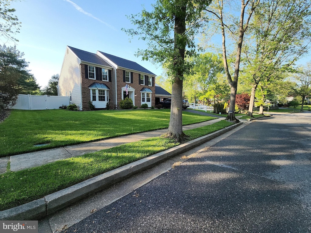 colonial home with brick siding, fence, and a front yard