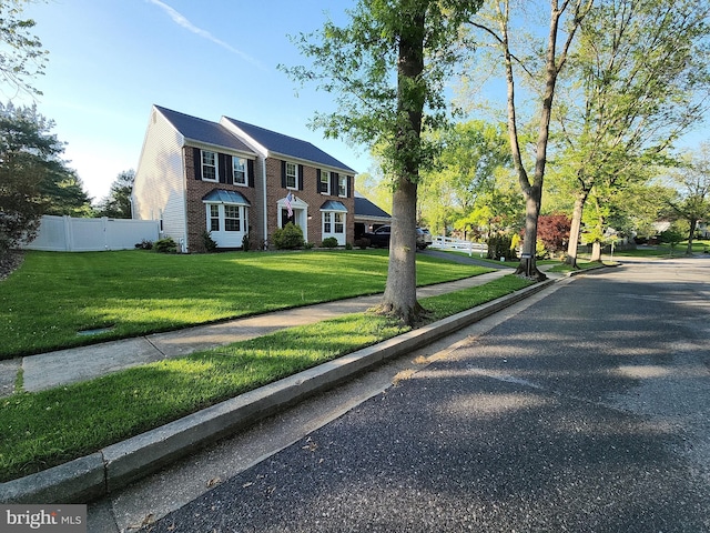 colonial home with brick siding, fence, and a front yard