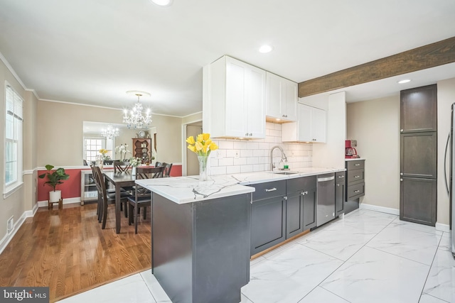 kitchen with appliances with stainless steel finishes, light stone countertops, a sink, white cabinets, and a notable chandelier