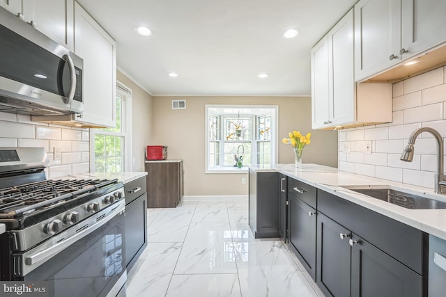 kitchen with visible vents, ornamental molding, baseboards, a sink, and appliances with stainless steel finishes