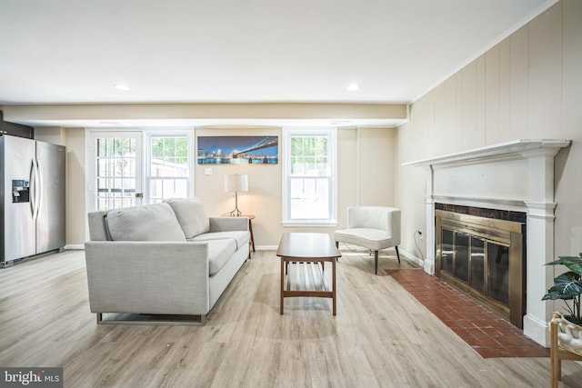 living room featuring a fireplace with flush hearth, baseboards, light wood-style flooring, and a wealth of natural light