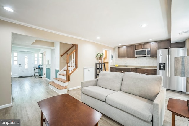 living area featuring visible vents, crown molding, stairs, baseboards, and light wood finished floors