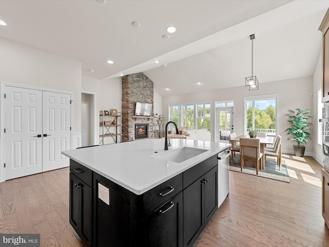 kitchen with dark cabinetry, a stone fireplace, a sink, and light wood finished floors