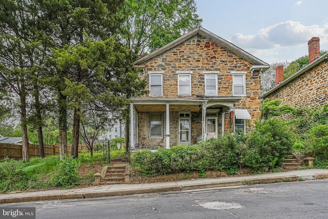 traditional home with stone siding, fence, covered porch, and stairs