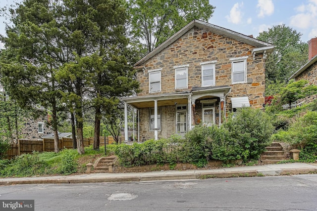 view of front of property with stone siding, fence, stairs, and a porch