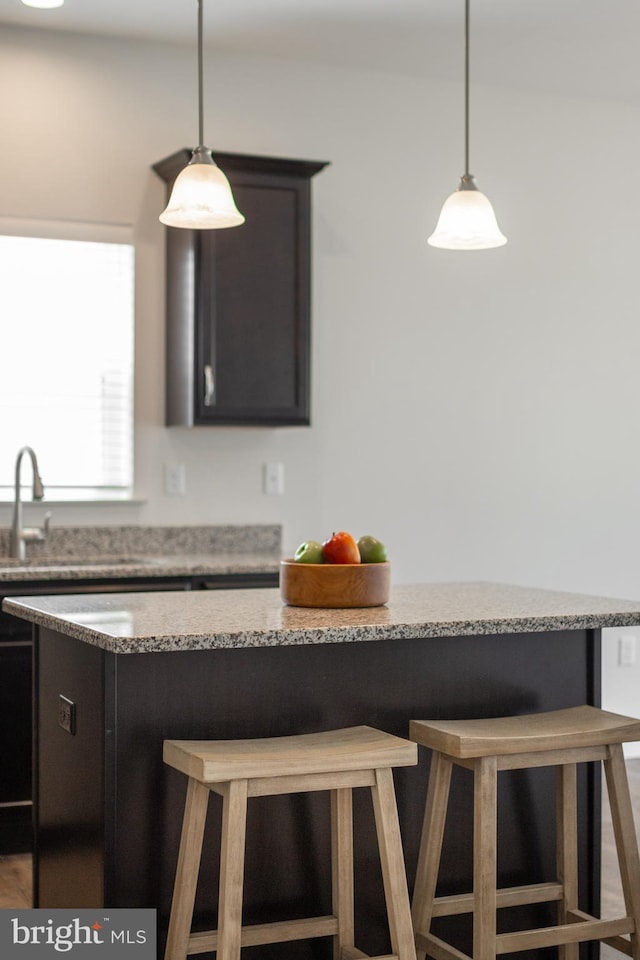 kitchen featuring light stone counters, a sink, decorative light fixtures, and a breakfast bar