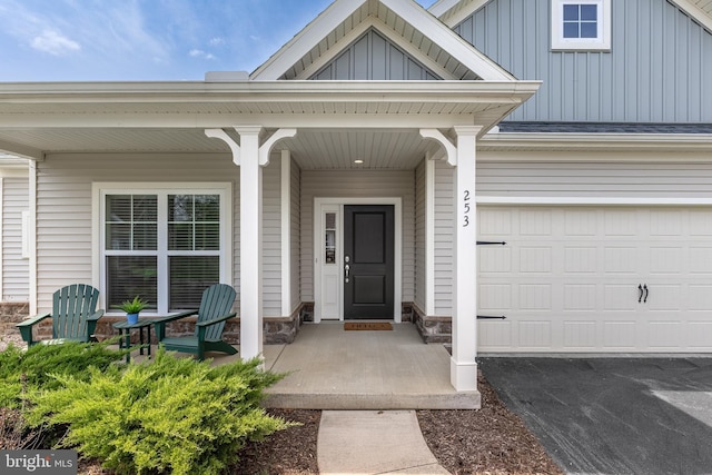 entrance to property with a porch, board and batten siding, driveway, and stone siding
