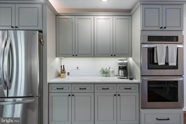 kitchen featuring light stone counters, gray cabinets, backsplash, and stainless steel appliances