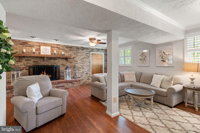 living area featuring plenty of natural light, a brick fireplace, a textured ceiling, and wood finished floors