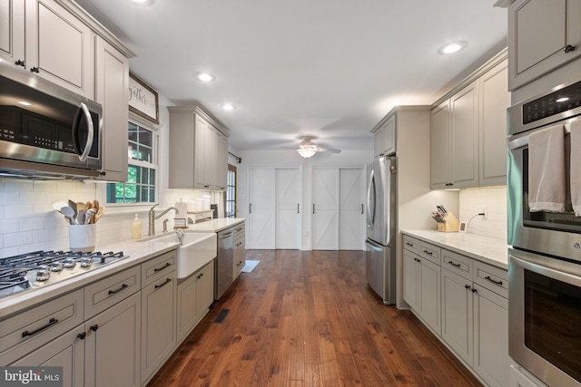 kitchen featuring decorative backsplash, a sink, gray cabinets, a ceiling fan, and appliances with stainless steel finishes