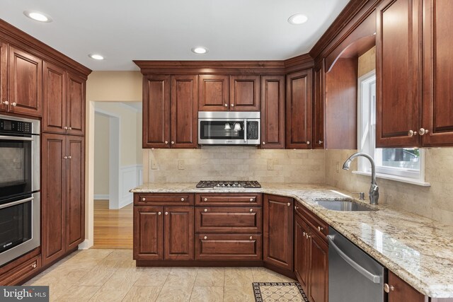 kitchen featuring stainless steel appliances, light stone counters, decorative backsplash, and a sink