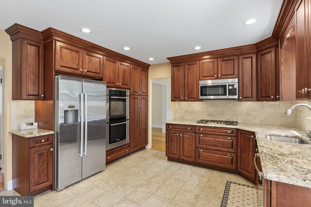 kitchen featuring stainless steel appliances, light stone counters, a sink, and tasteful backsplash