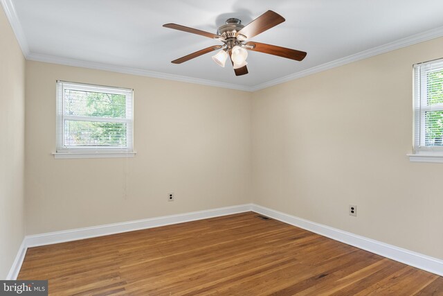 spare room with a ceiling fan, baseboards, wood finished floors, visible vents, and ornamental molding