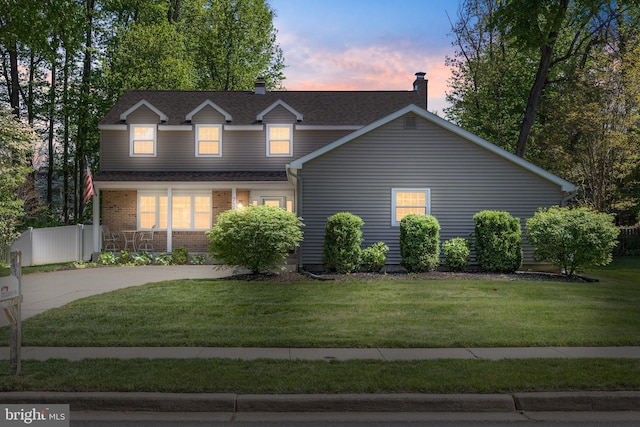 traditional-style house featuring covered porch, a chimney, a front yard, roof with shingles, and concrete driveway