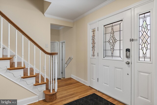 foyer entrance featuring crown molding, baseboards, stairs, and light wood-type flooring