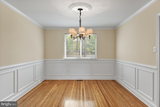 unfurnished dining area featuring crown molding, light wood-style flooring, a wainscoted wall, and a notable chandelier