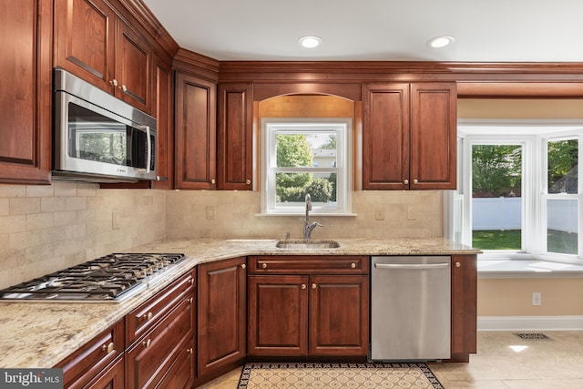 kitchen featuring baseboards, light stone counters, a sink, backsplash, and stainless steel appliances