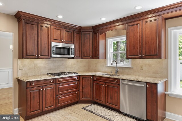 kitchen featuring backsplash, appliances with stainless steel finishes, a sink, and light stone counters