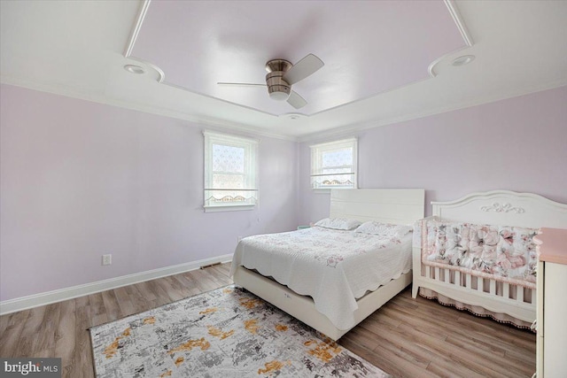 bedroom featuring a raised ceiling, ornamental molding, a ceiling fan, and wood finished floors