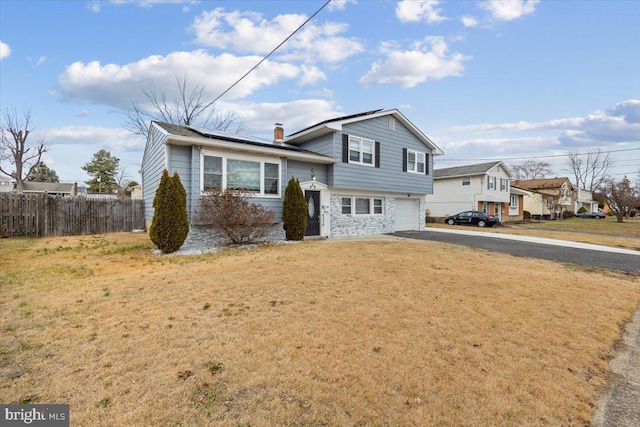 split level home with fence, a garage, a front yard, roof mounted solar panels, and driveway