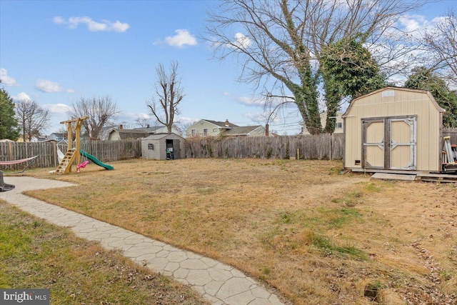 view of yard with a storage shed, an outbuilding, a fenced backyard, and a playground