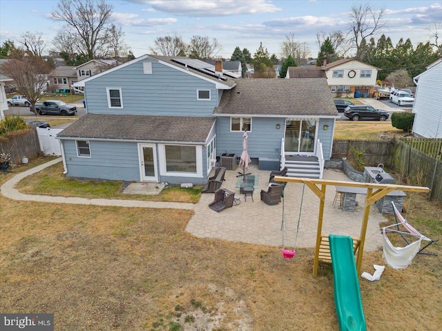 back of property featuring a shingled roof, central AC, a fenced backyard, roof mounted solar panels, and a patio area