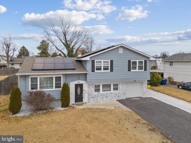tri-level home featuring solar panels, a front yard, a garage, aphalt driveway, and stone siding