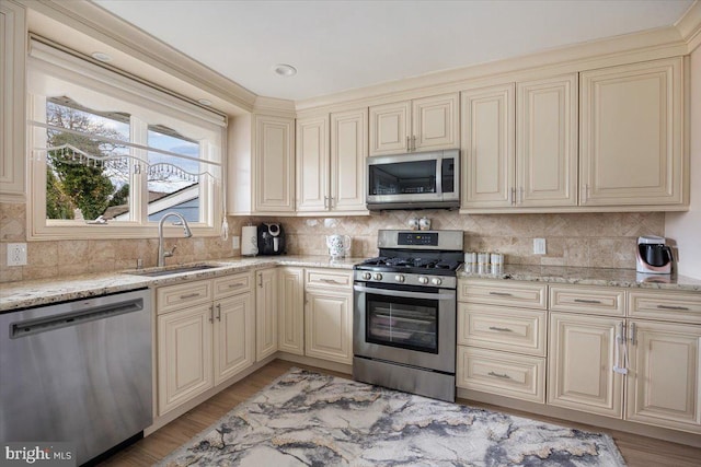 kitchen featuring cream cabinets, light stone countertops, a sink, stainless steel appliances, and tasteful backsplash
