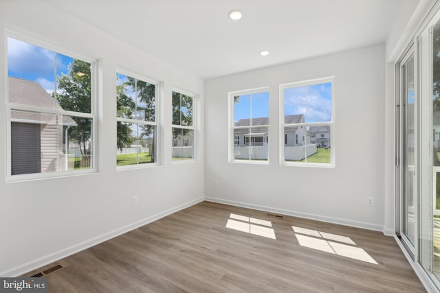 unfurnished sunroom with baseboards, wood finished floors, and a healthy amount of sunlight